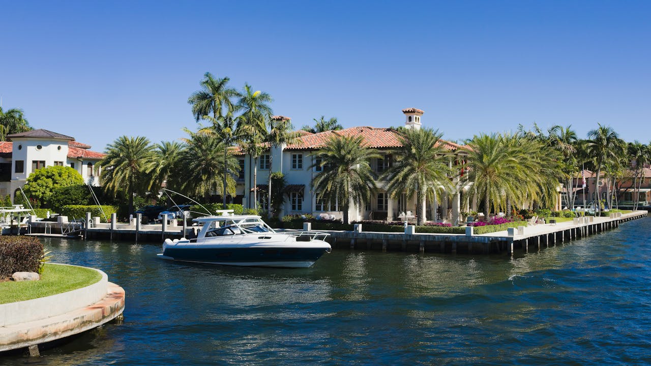 Stunning view of a luxury villa with boat in Fort Lauderdale's picturesque canal under a clear blue sky.